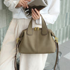 Person holds a taupe leather handbag with gold hardware, wearing a white top and beige pants.