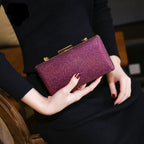 A person holds a sparkling purple clutch with gold accents, wearing a black outfit and maroon nails.