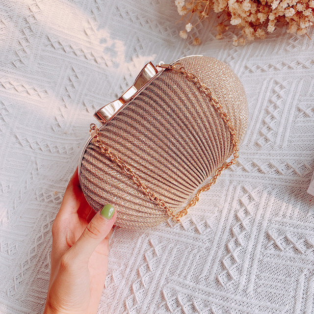 Gold textured clutch with a bow clasp and chain, held on a white patterned background.