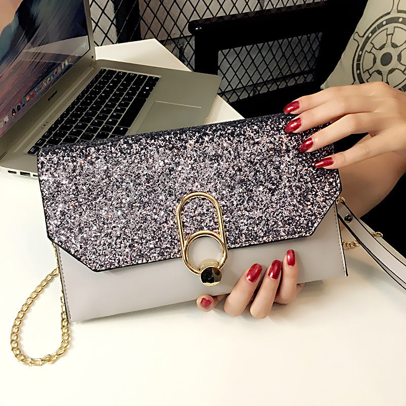 Silver glitter clutch with a gold clasp, held by a person with red nails, near a laptop.
