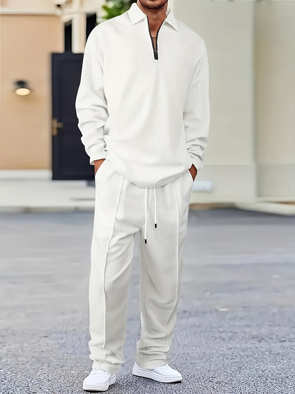 Man in a white, textured tracksuit with a half-zip collar, standing on a gray pavement.