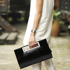 Woman in white outfit holding a black textured clutch with a cutout handle outdoors.