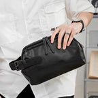 Person in white shirt holding a black leather pouch with a buckle and zipper detail.