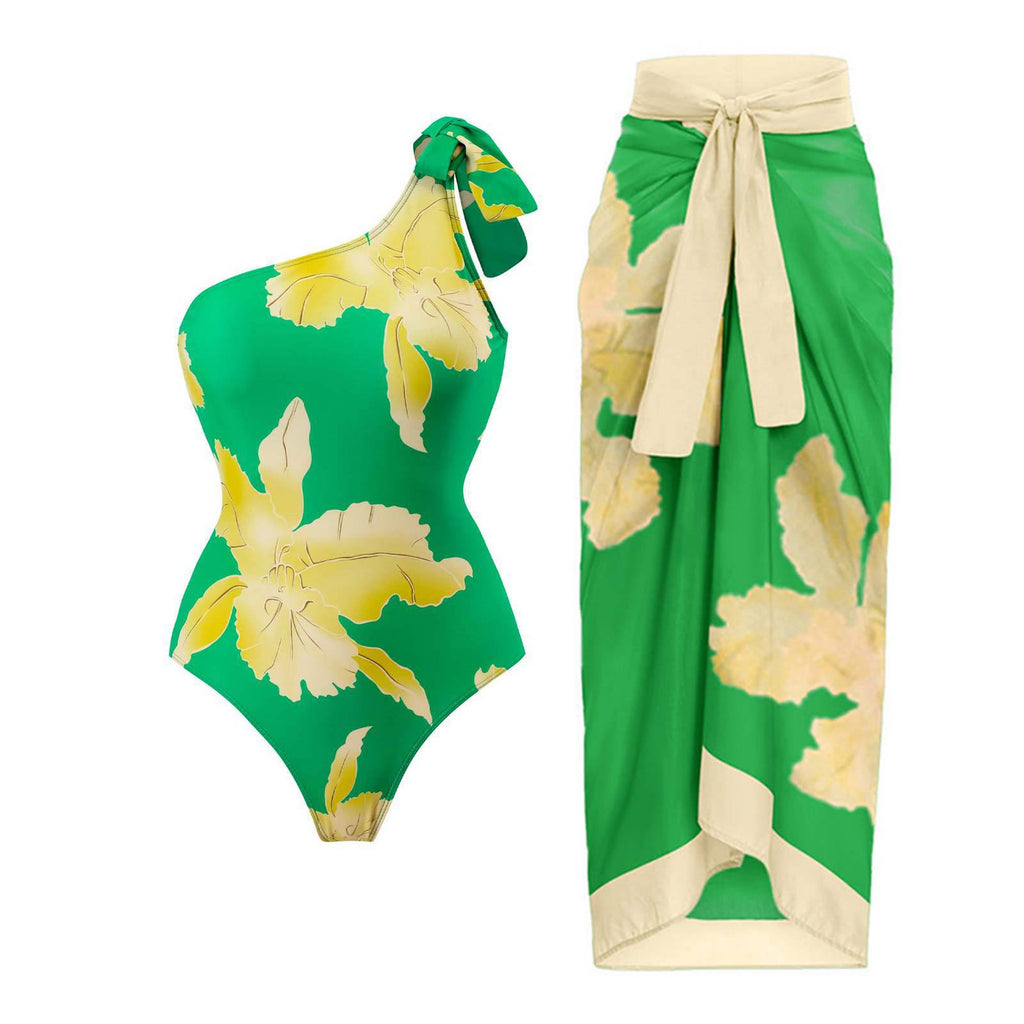 Green one-shoulder swimsuit and matching wrap skirt with large yellow floral patterns.