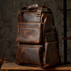 Brown leather backpack with gold zippers and multiple pockets, set against a textured gray background.