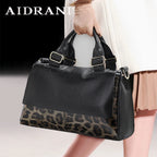 Black leather handbag with leopard print bottom, held by a person wearing a beige coat and gloves.