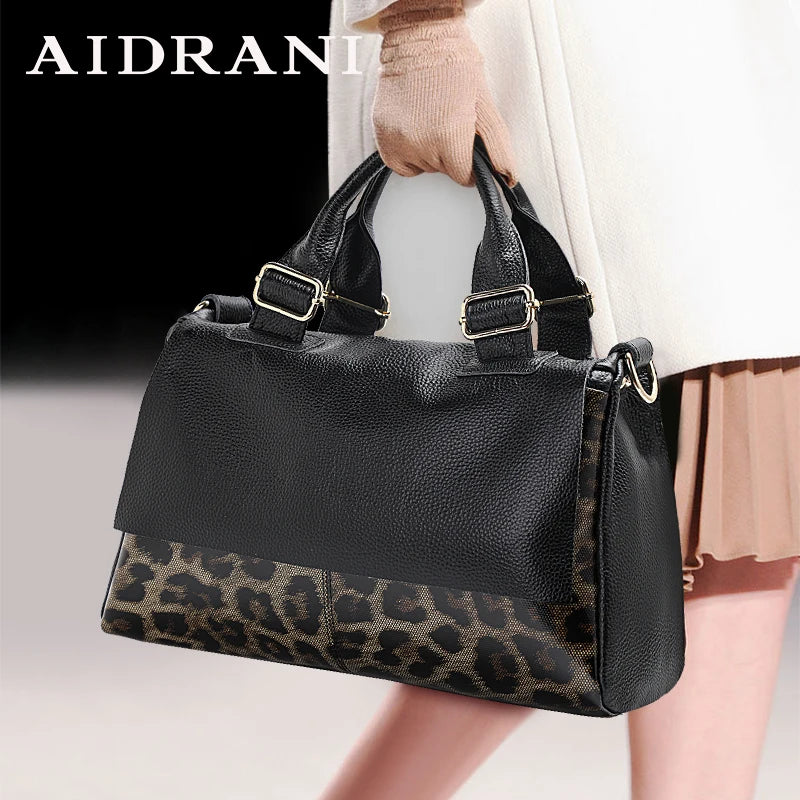 Black leather handbag with leopard print bottom, held by a person wearing a beige coat and gloves.