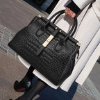 Person holding a large black crocodile-patterned handbag with gold accents, wearing a white coat.