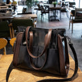 Black leather handbag with brown straps on a wooden table in a cafe setting.