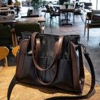 Black leather handbag with brown straps on a wooden table in a cafe setting.