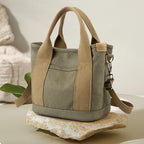 Green canvas tote with tan handles and strap, resting on a stone slab.
