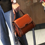 Person holding a small, orange leather handbag with a striped shoulder strap and wearing a watch.